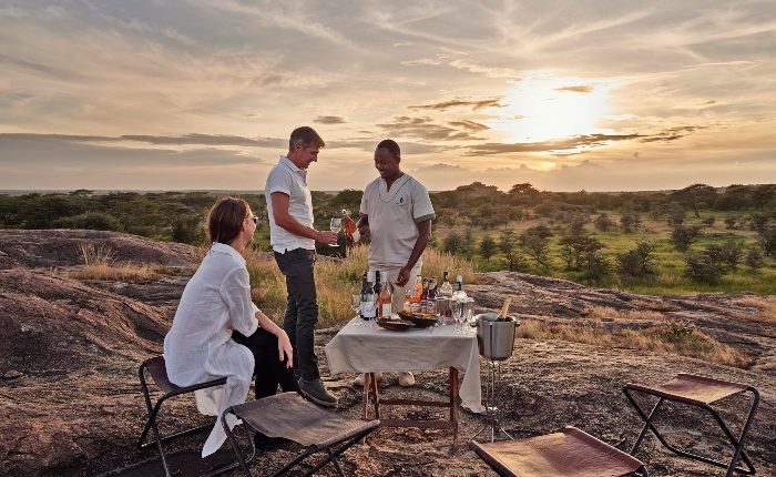 A couple enjoying a scenic sundowner with a safari guide, overlooking breathtaking African landscapes.